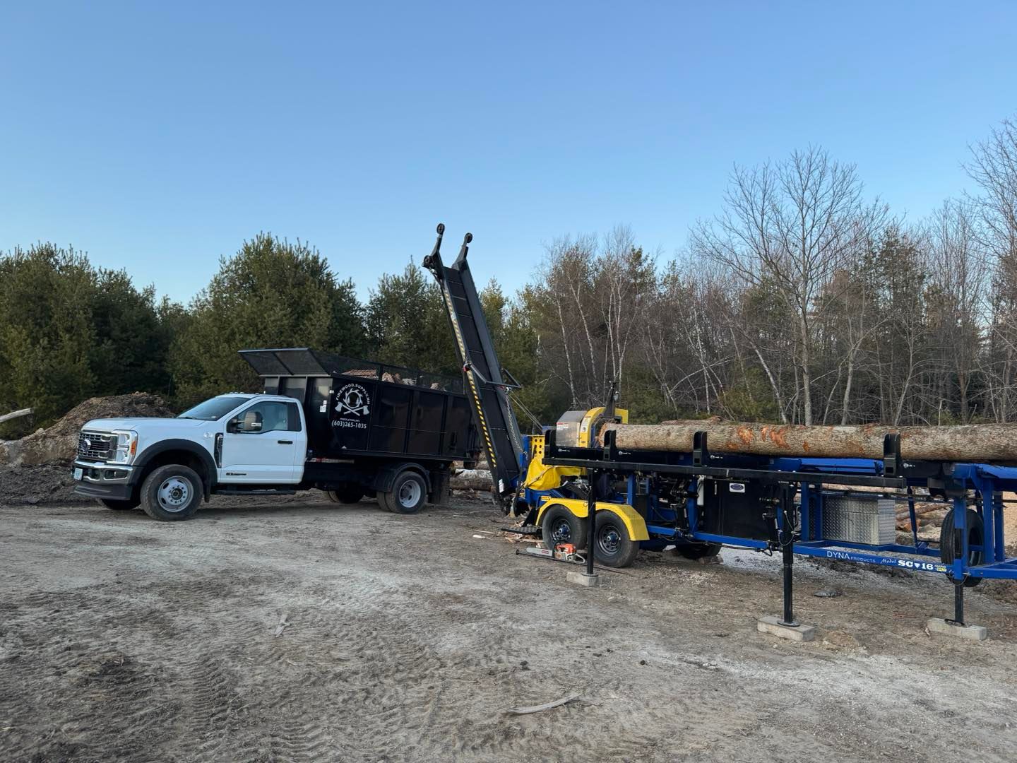 A white truck is parked next to a machine that is cutting logs.