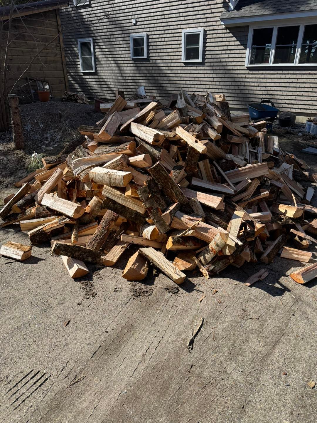 A pile of wood is sitting on the ground in front of a house.