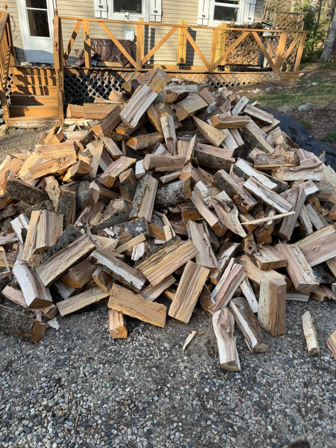 A pile of wood is sitting on the ground in front of a house.