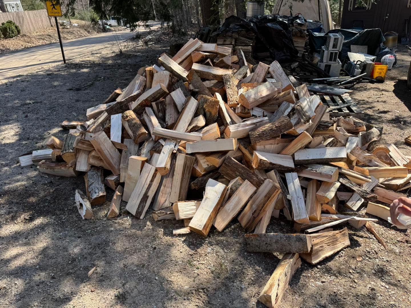 A pile of wood is sitting on the ground next to a road.
