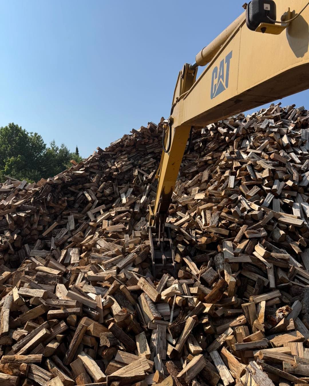 A large pile of wood is being loaded by a cat excavator