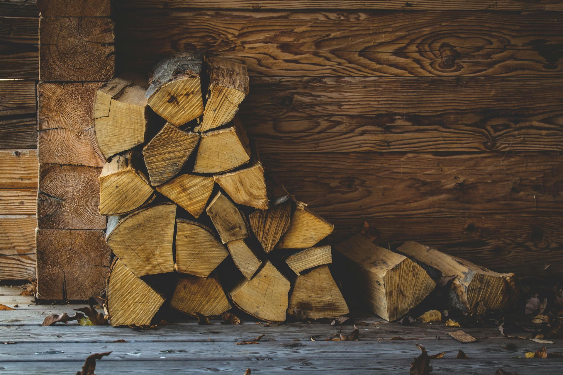 Stacked split firewood against a wooden wall and gray floor indoors