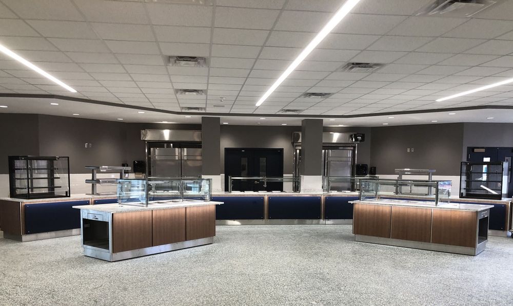 Woman in straw hat smiles, holding wine glass near a lake.