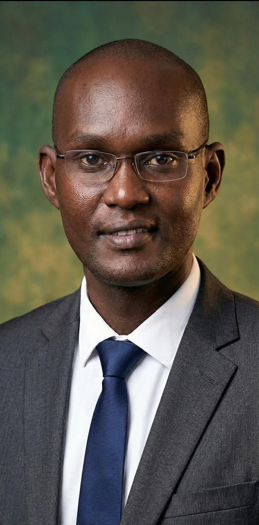 Man in a suit and glasses, smiling, facing the camera.