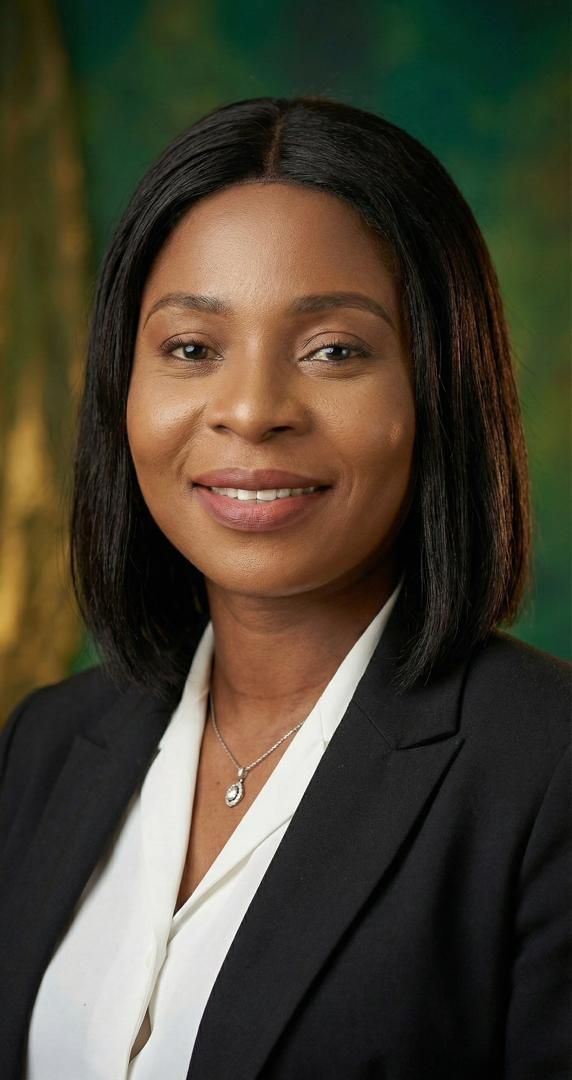 Woman in a blazer and white top smiles, posing in front of a green background.