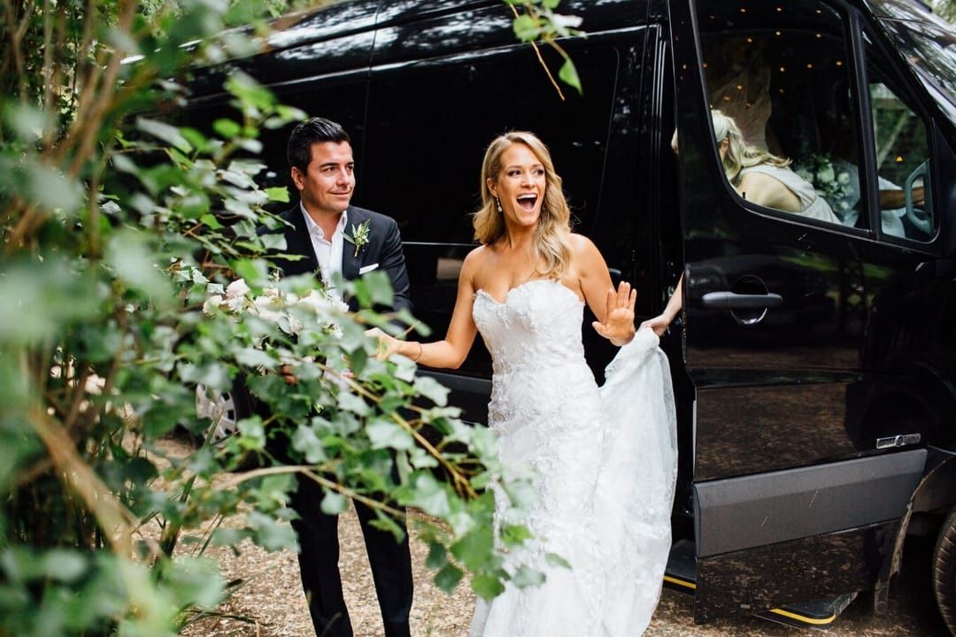 A bride in a veil is sitting in a car looking out the window.