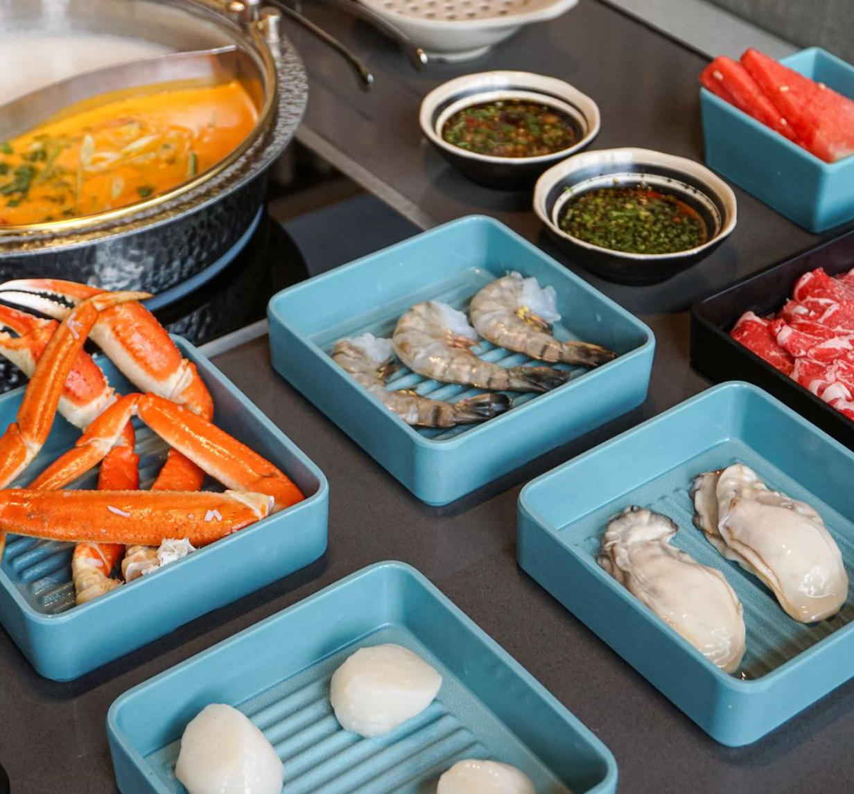 A table topped with trays of food including crab legs and shrimp