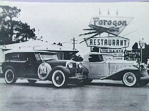 two old cars are parked in front of a paragon restaurant