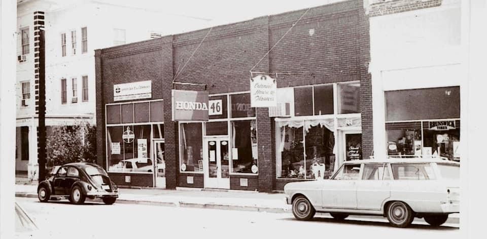a black and white photo of a store front with a car parked in front of it