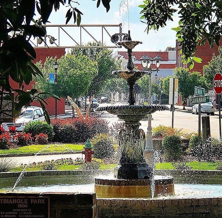 a fountain in triangle park with a stop sign in the background