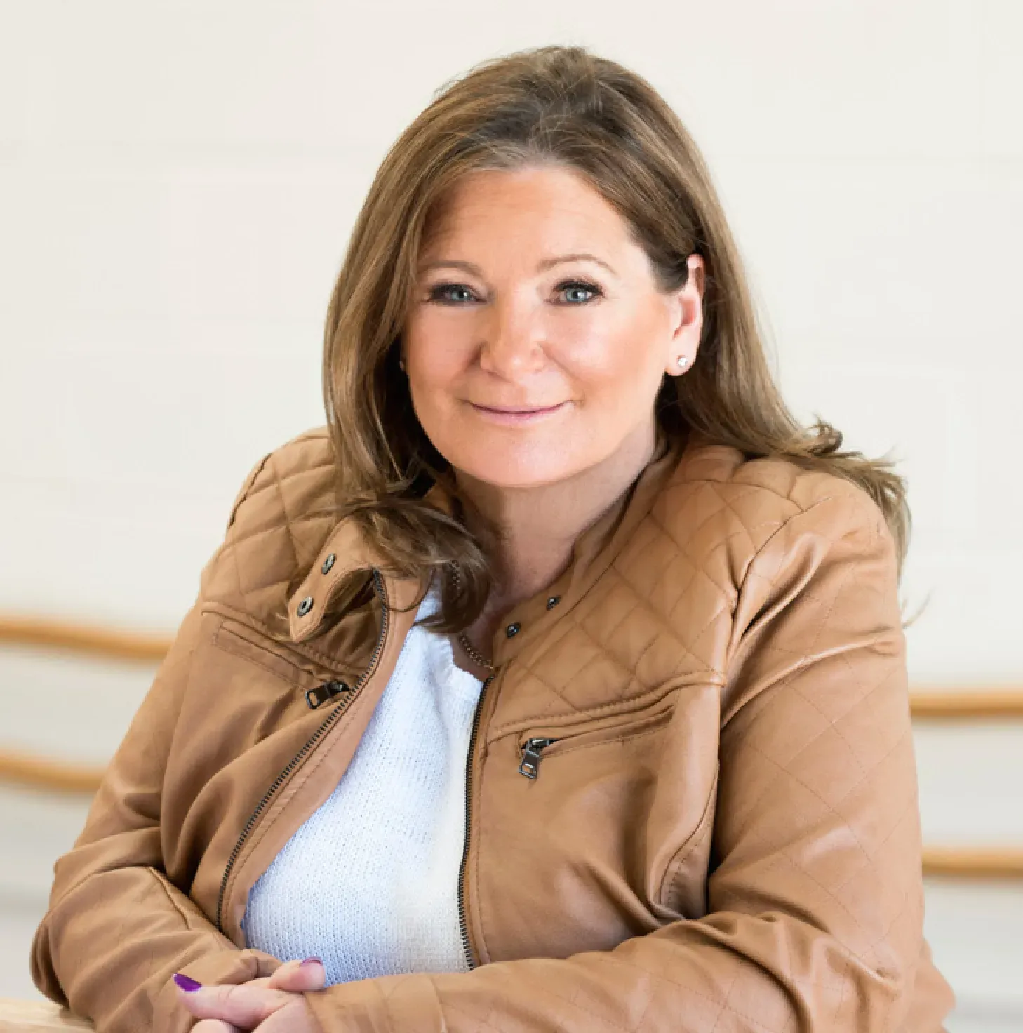 Woman with brown hair, wearing a brown leather jacket and white top, smiling.