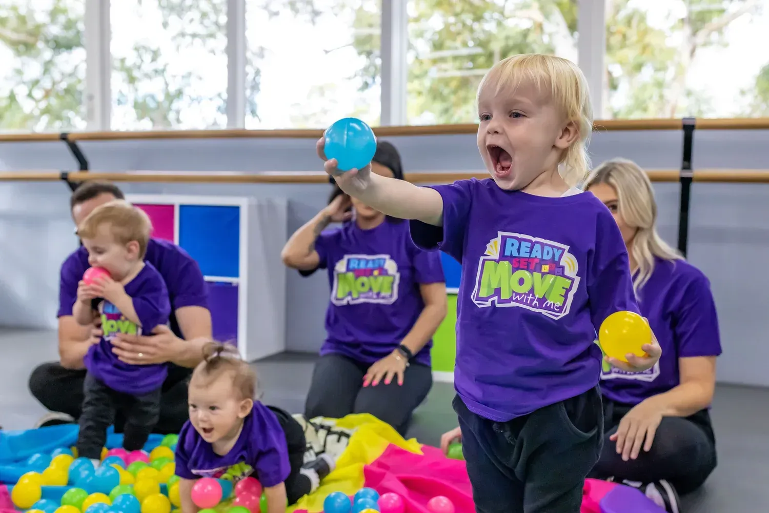 Children in purple shirts playing with balls in a brightly lit dance studio.