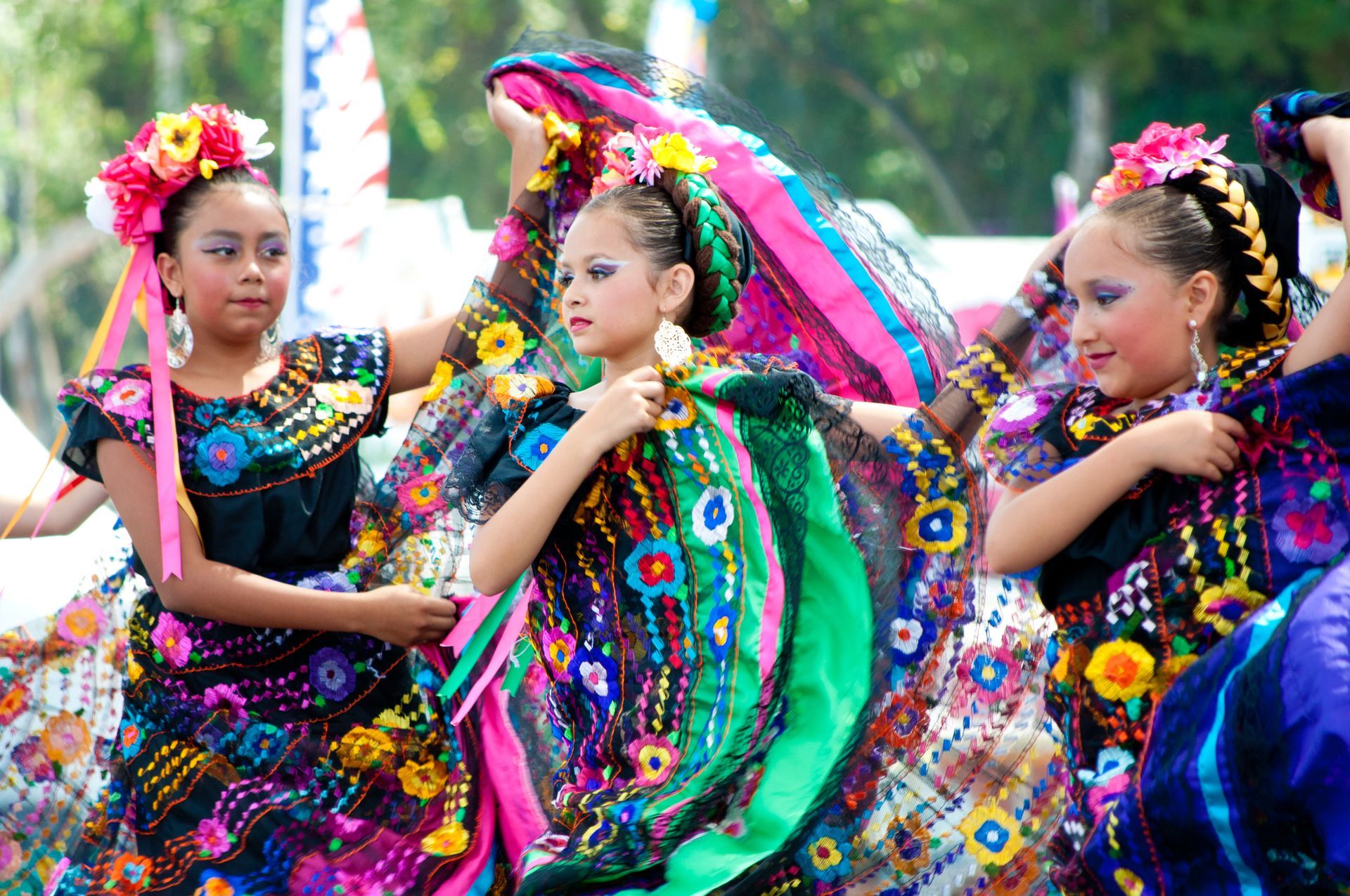 Young girls in colorful traditional dresses dance outdoors, smiling.