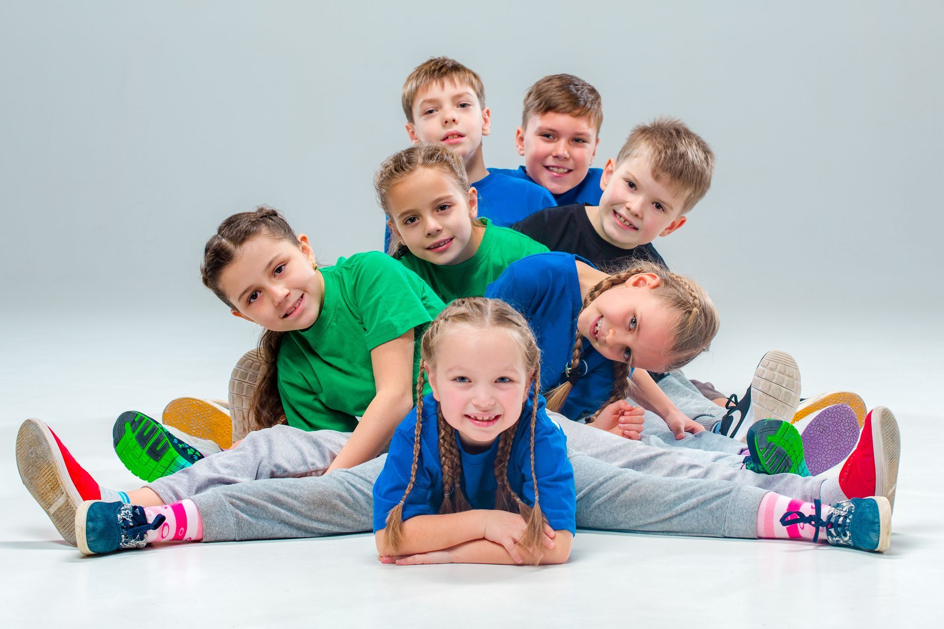 Group of smiling children in colorful shirts and gray sweatpants, posed together.