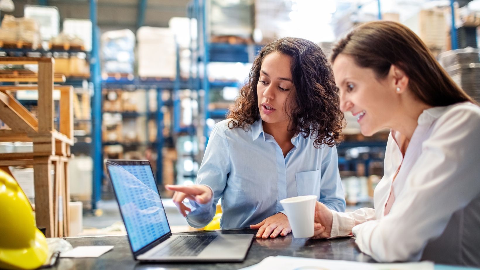 Two women are sitting at a table looking at a laptop computer.