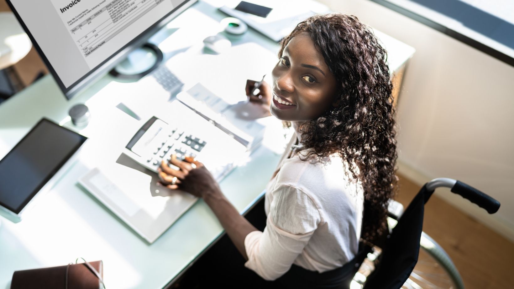 Image of a woman in a wheelchair working in front of an office computer. 