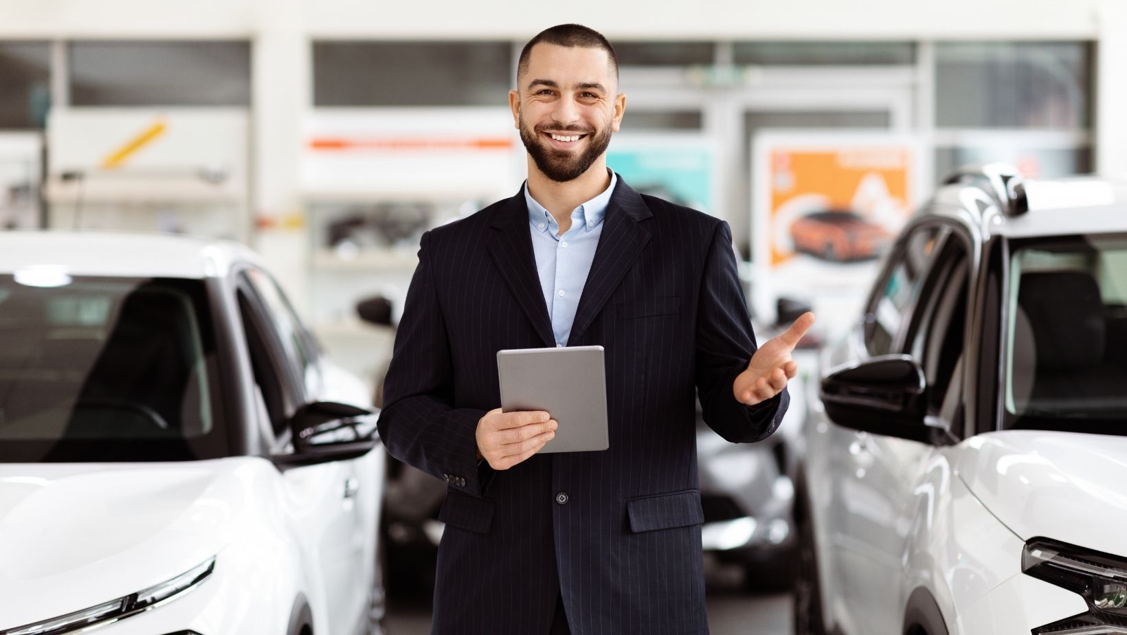 A man in a suit is holding a tablet in a car showroom.