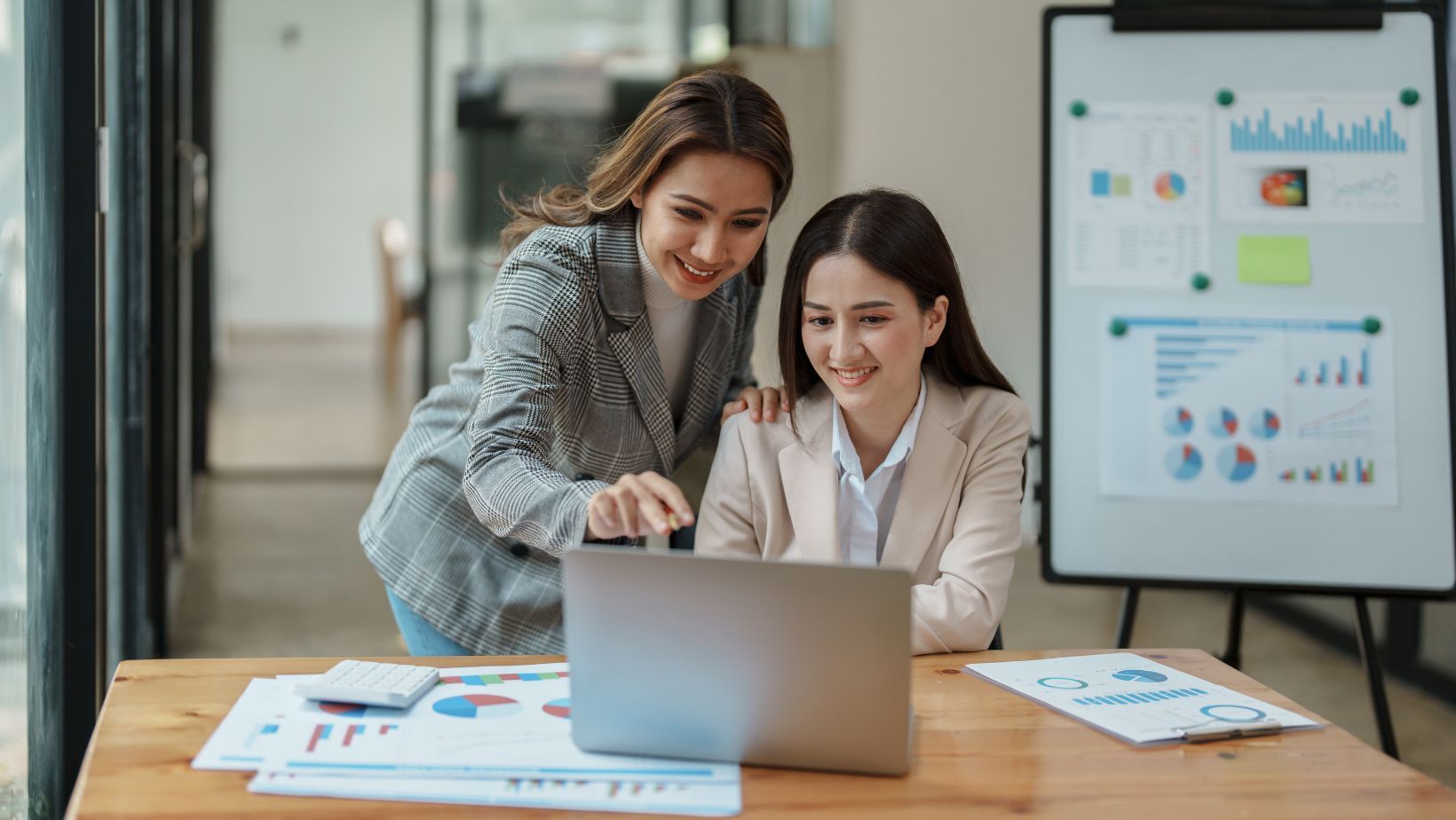 Two women are sitting at a table looking at a laptop computer.