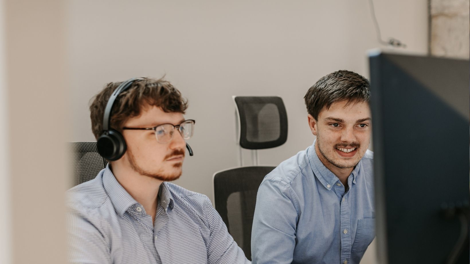 Two men wearing headphones are looking at a computer screen.