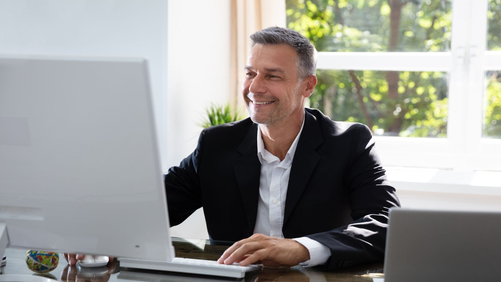 A man in a suit is sitting at a desk in front of a computer.