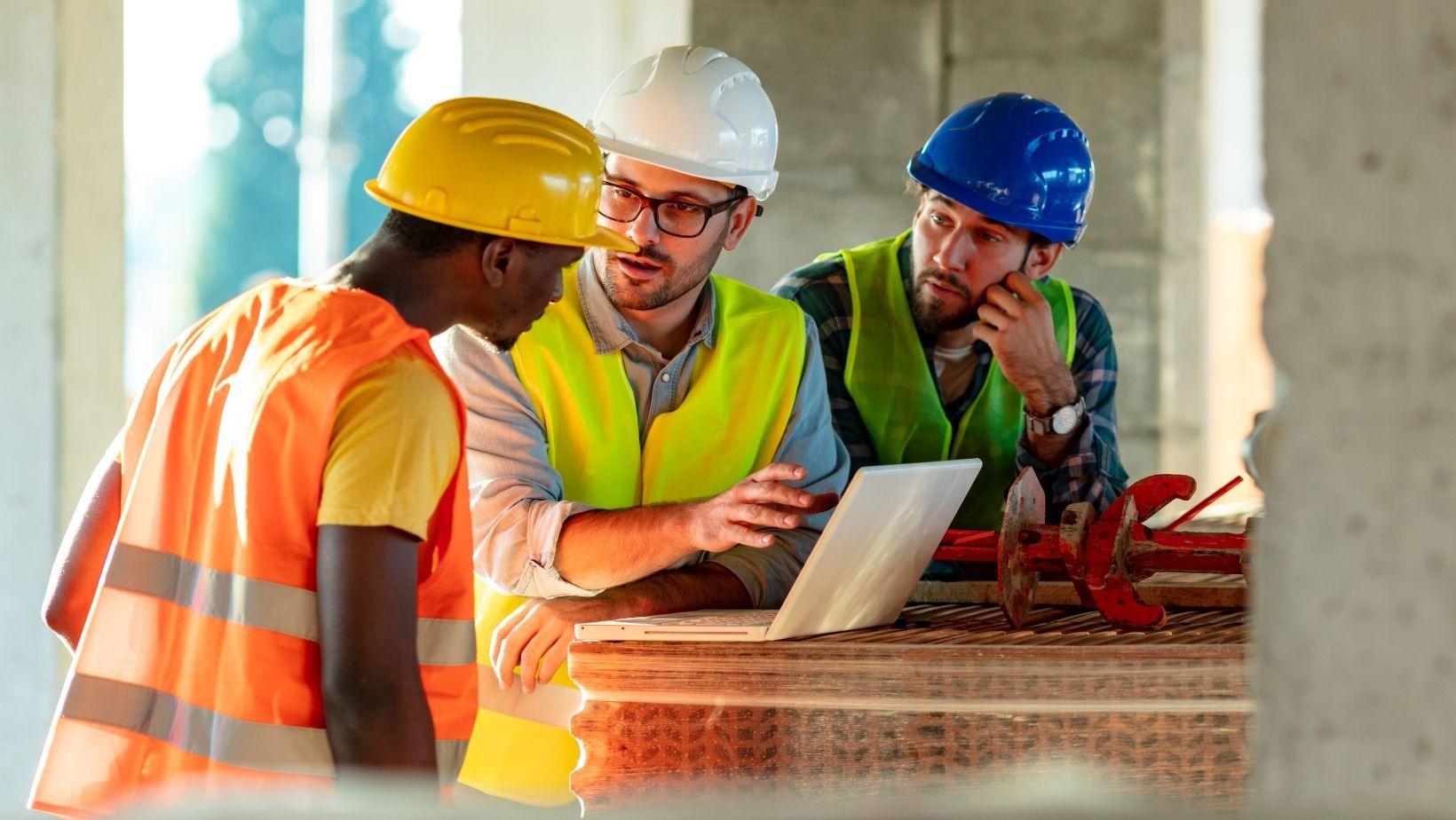 A group of construction workers are looking at a laptop on a construction site.