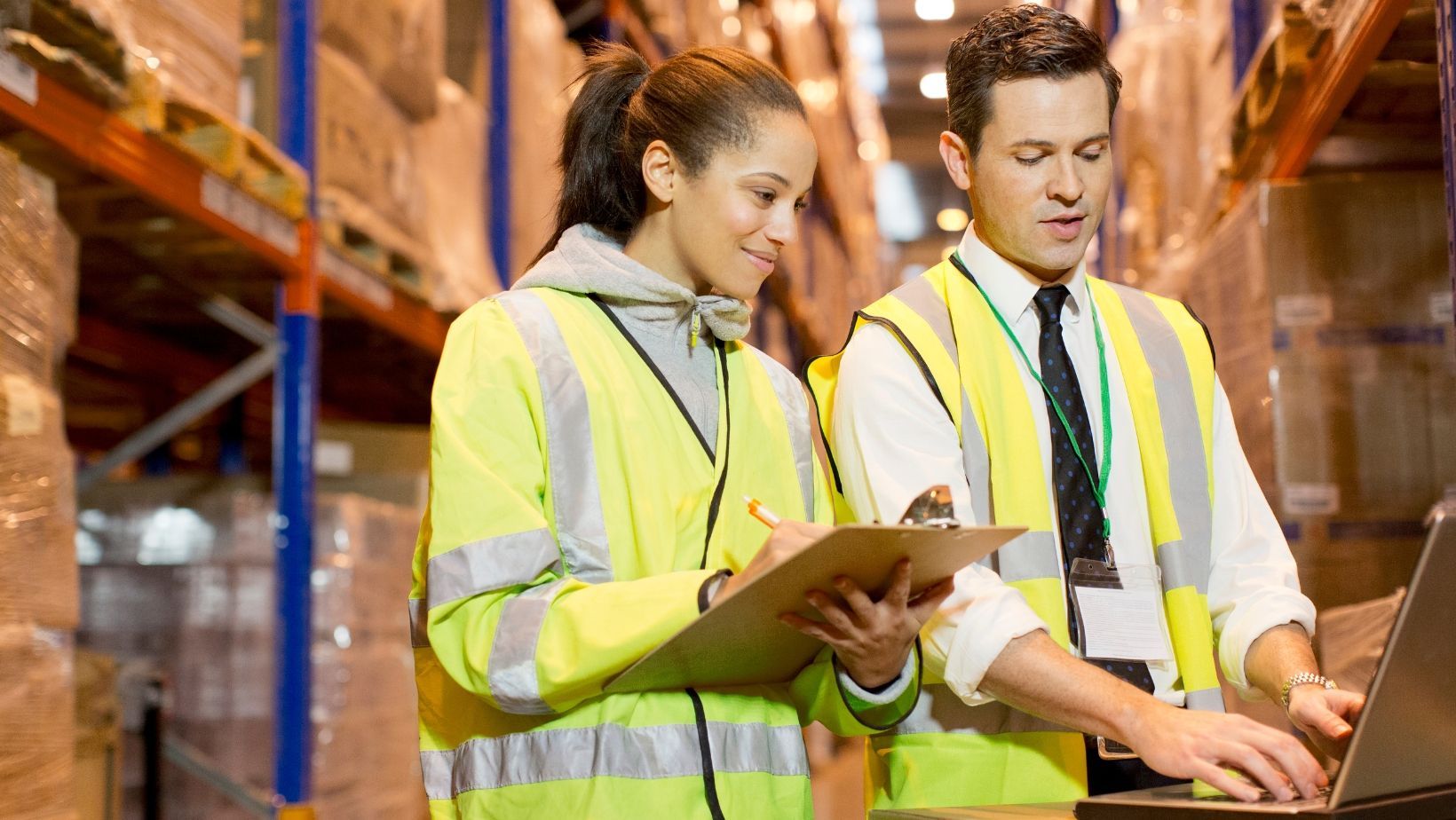 A man and a woman are looking at a laptop in a warehouse.