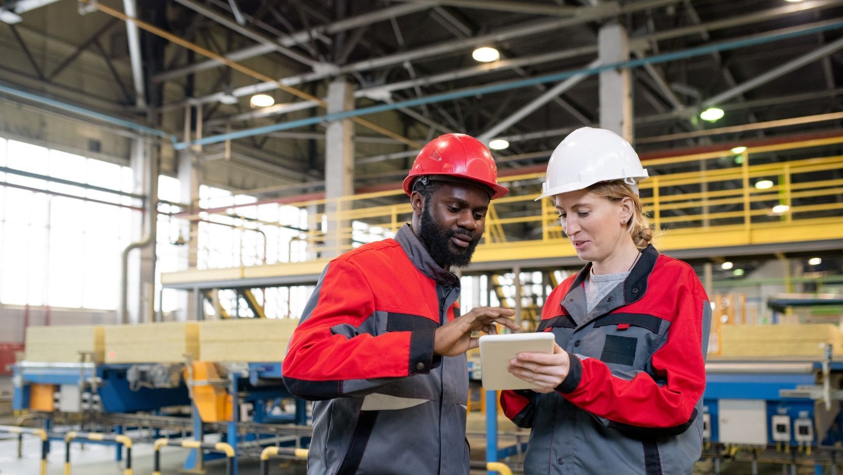 A man and a woman are looking at a tablet in a factory.