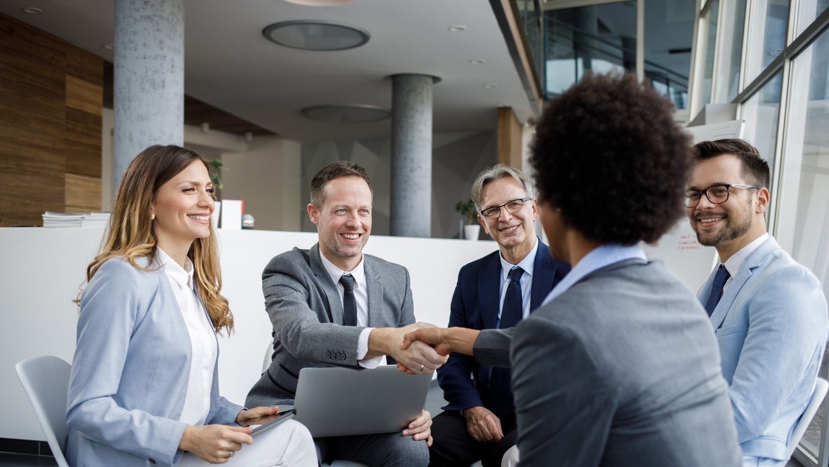 A group of business people are sitting around a table shaking hands.