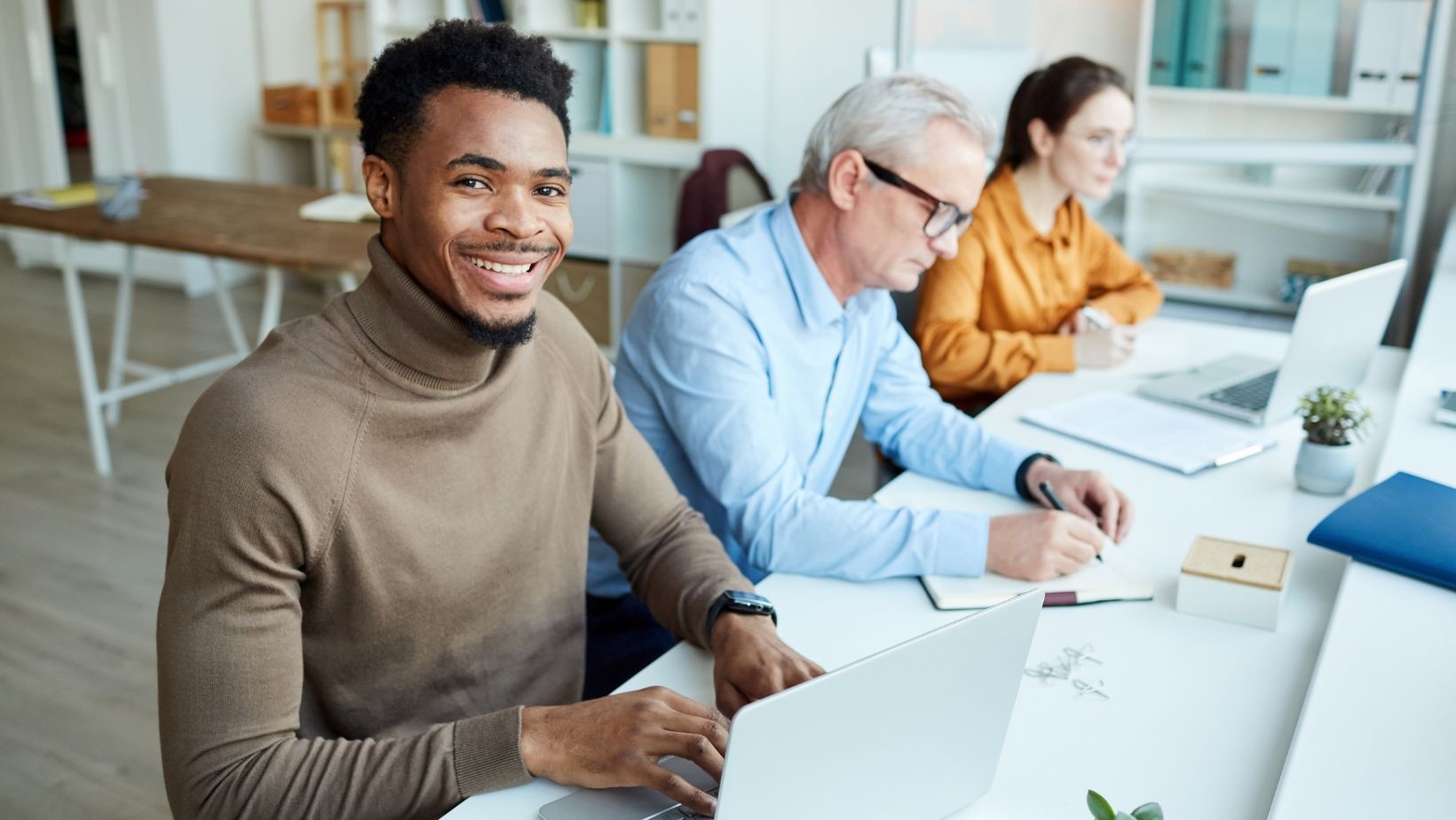 A group of people are sitting at desks with laptops in an office.