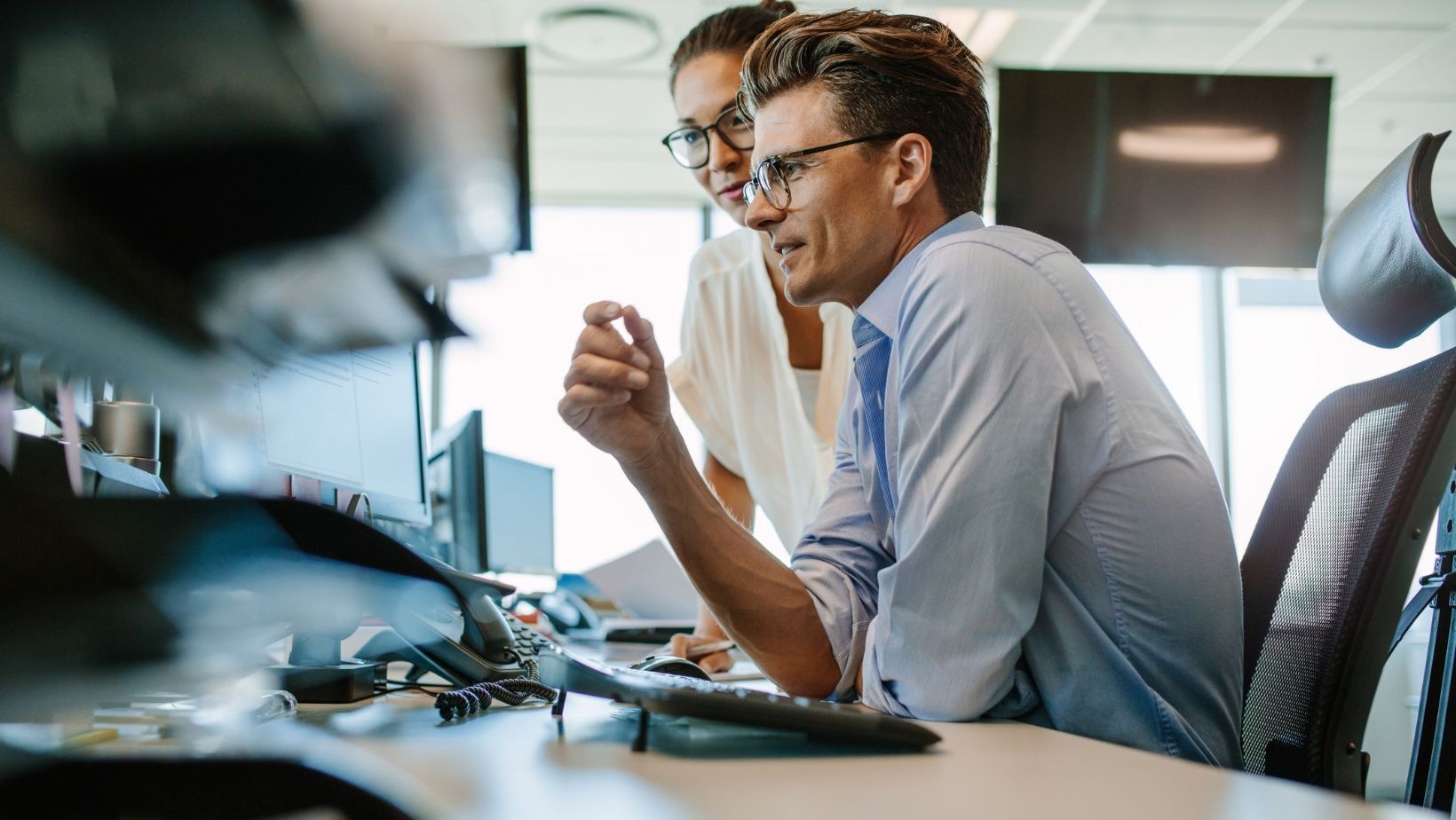 A man and a woman are looking at a computer screen in an office.