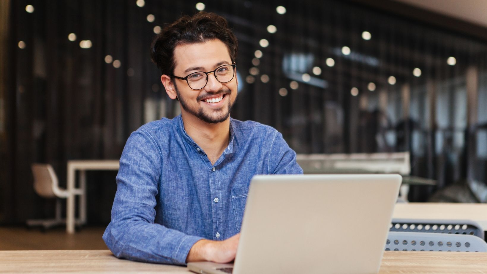 A man is sitting at a table using a laptop computer.