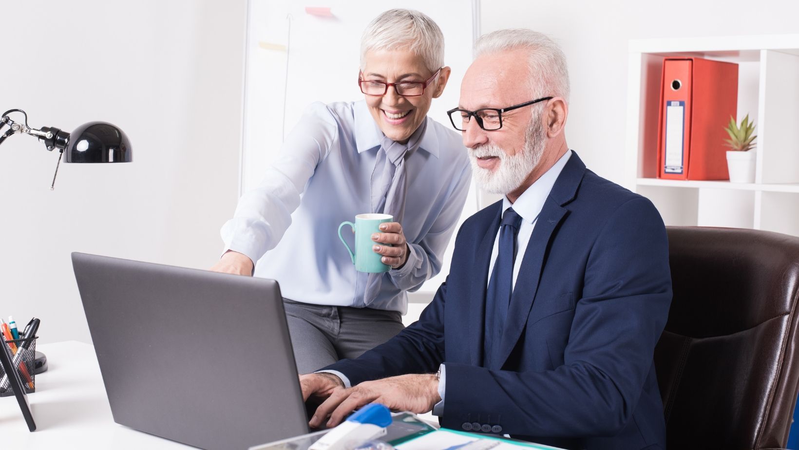 Two men are standing next to each other in front of a laptop computer.