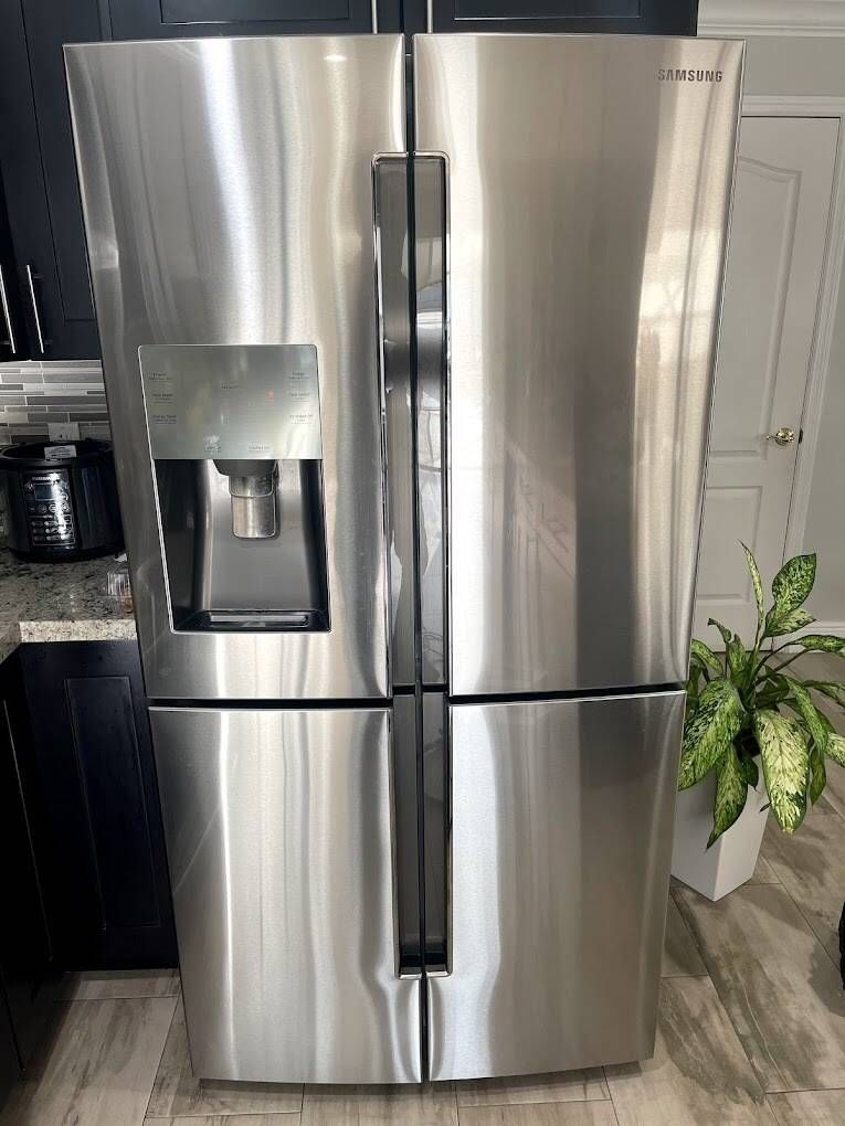 a stainless steel refrigerator is sitting in a kitchen next to a plant .