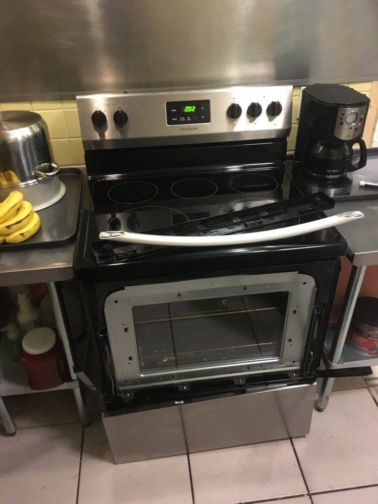a stove with the door open in a kitchen next to a coffee maker .