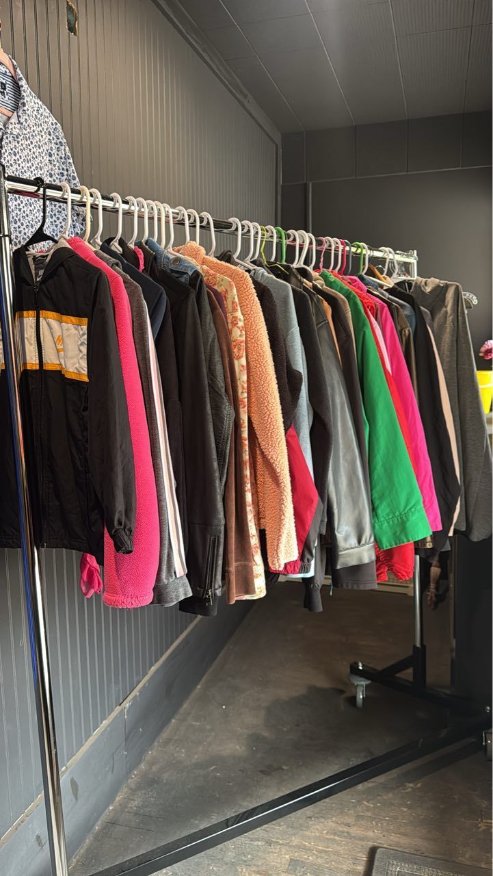 Clothing rack with assorted colorful sweaters and jackets in a narrow dark storage room