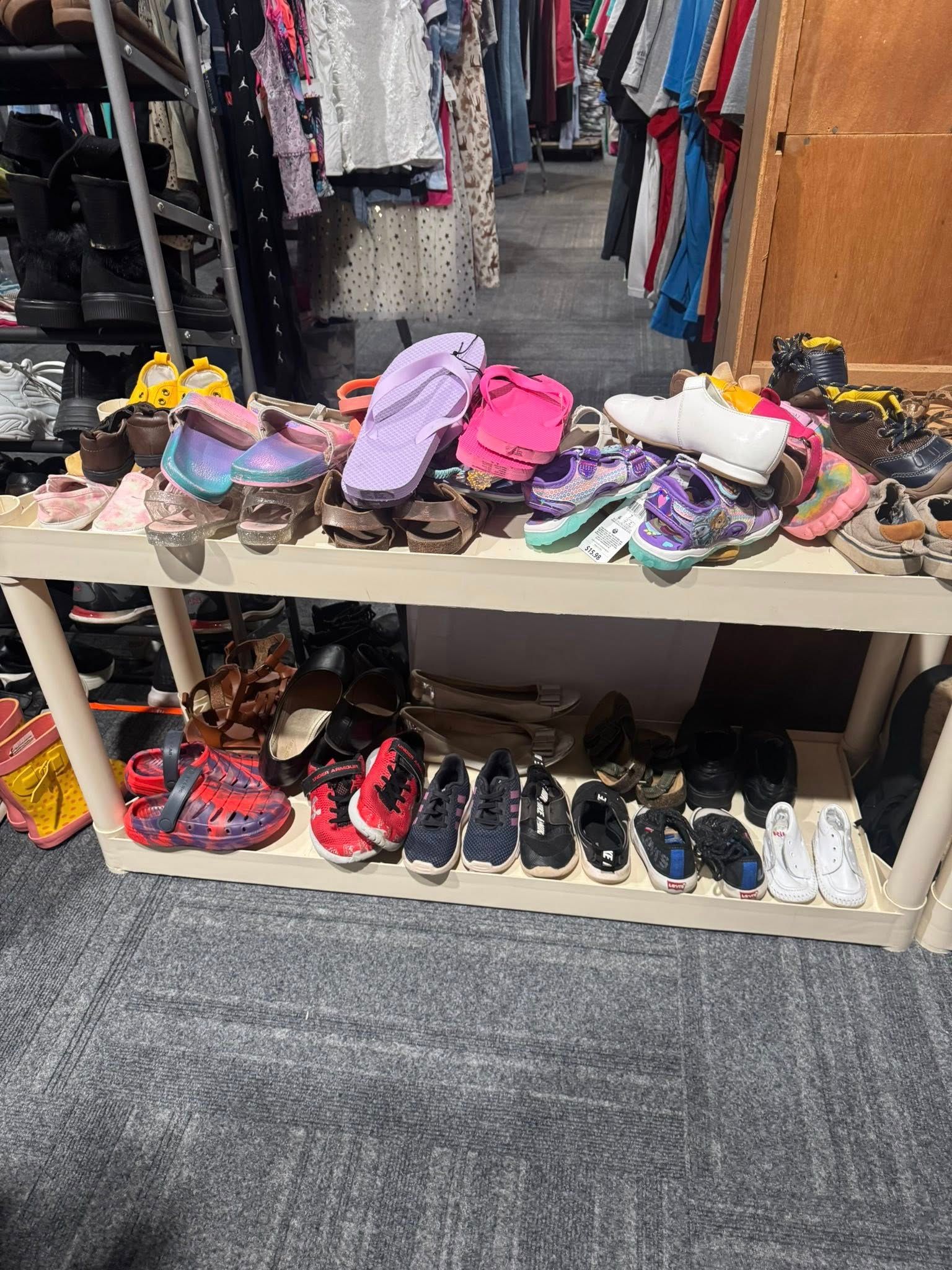Shelves of assorted shoes in a clothing store, with sandals and sneakers arranged on display.