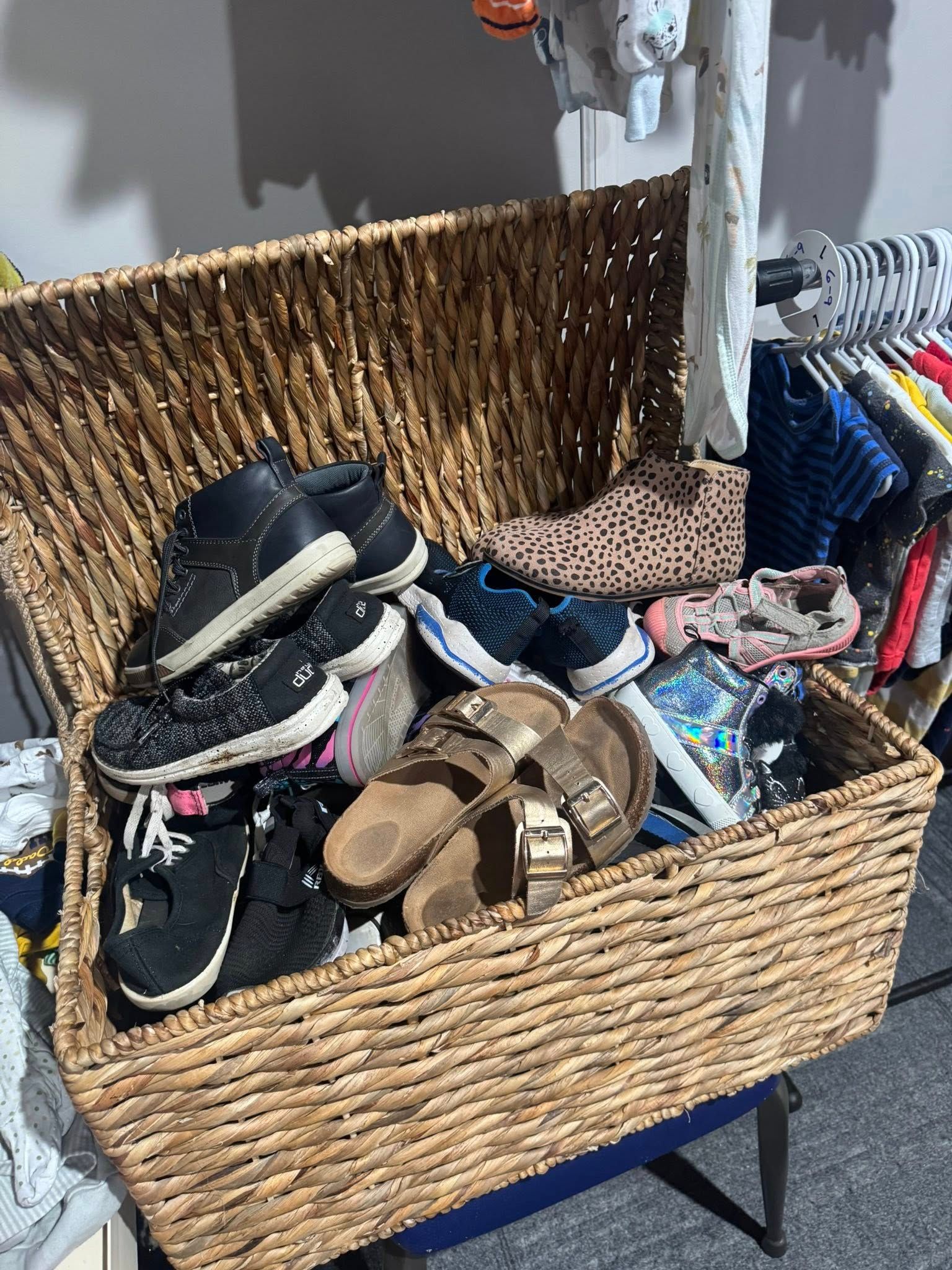 Wicker basket filled with assorted shoes and clothing items on a blue stand in a room