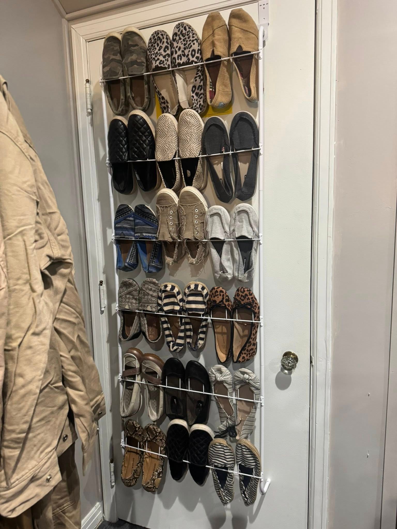 Shoes neatly hung on a white door, with a beige coat hanging beside them.