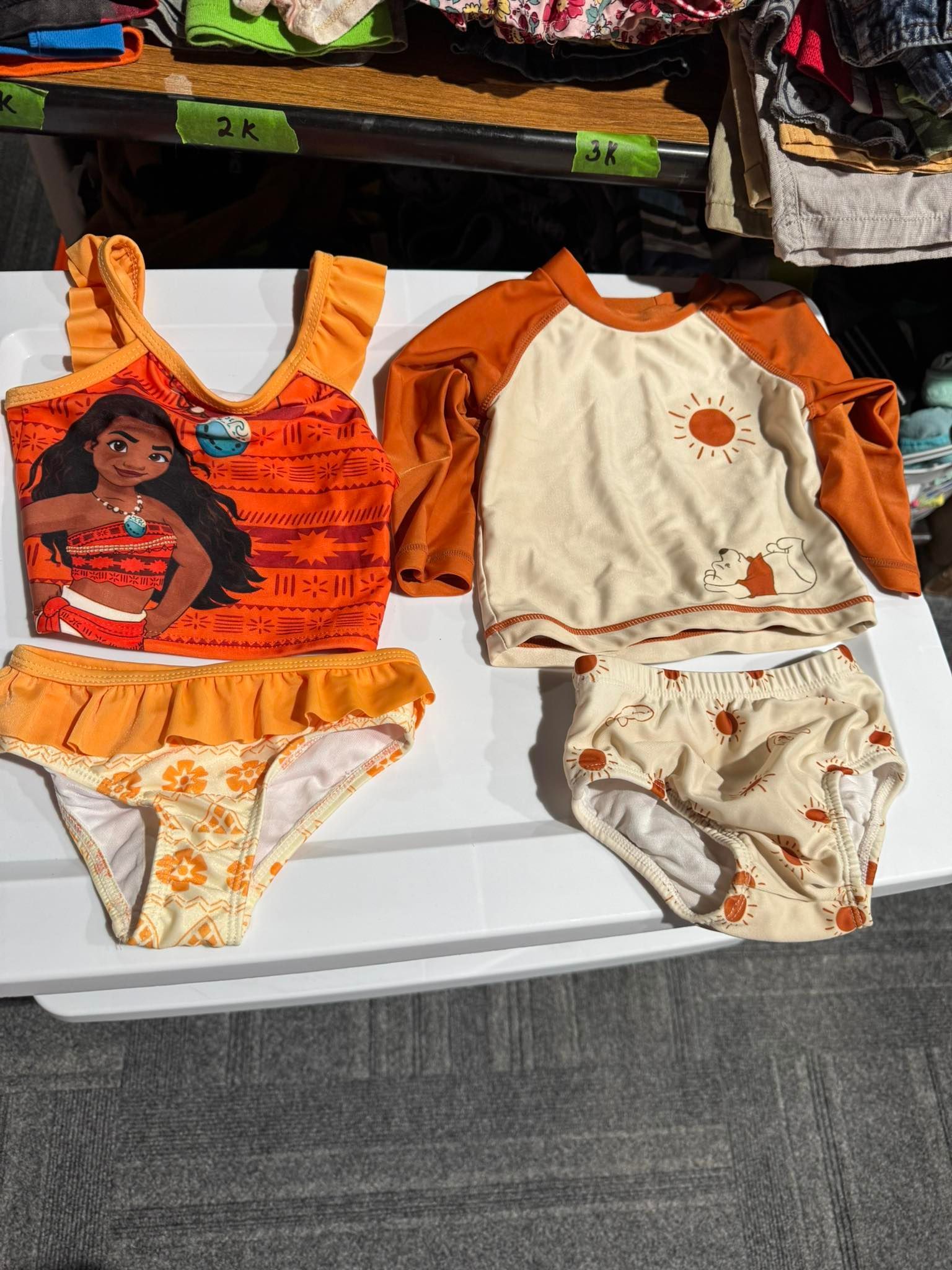 Two orange and cream baby outfits laid out side by side on a white table.
