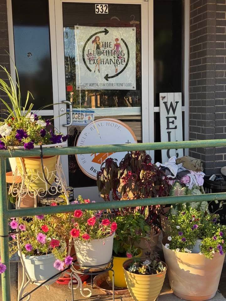 Flower-filled storefront with potted blooms, decorative sign, and a “WELCOME” sign by the entrance