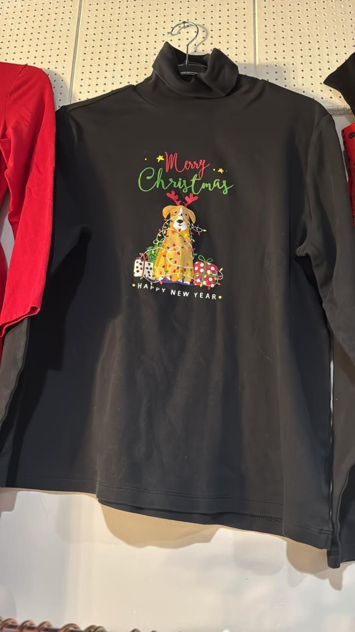 Black long-sleeve shirt with a festive cat graphic and holiday text hanging on a display rack
