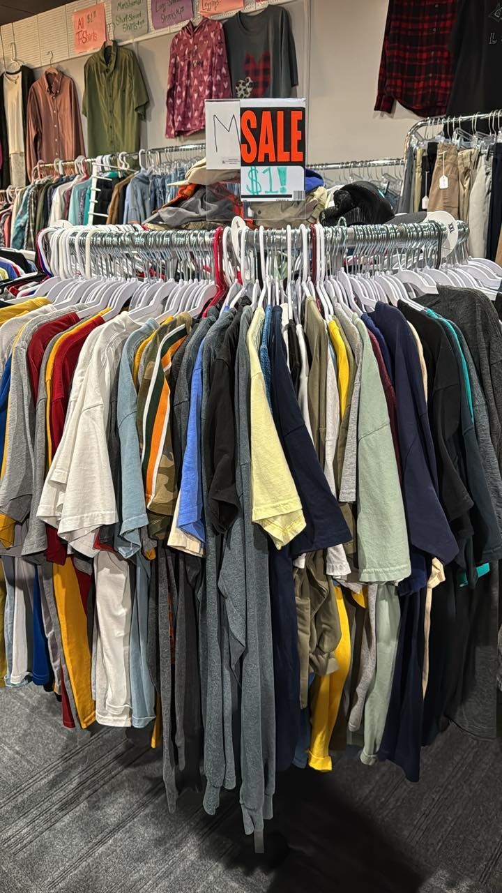 Racks of assorted clothing in a store with a red SALE sign above them