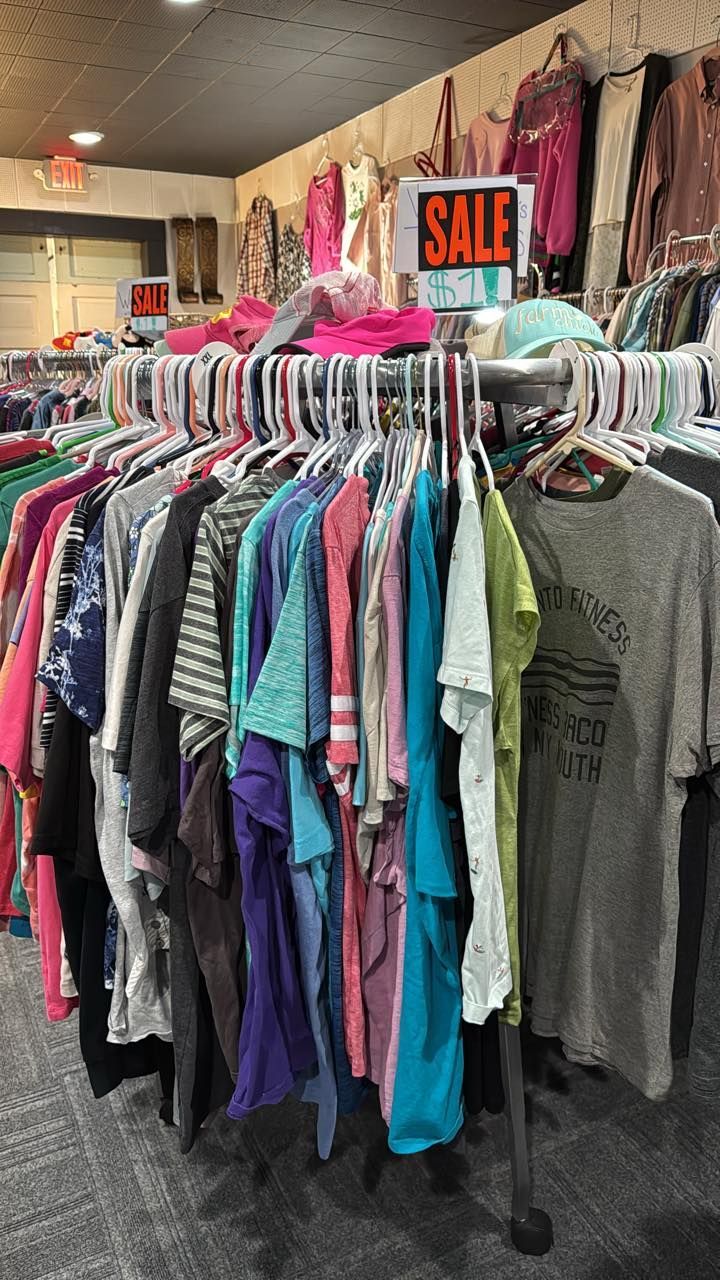 Clothing store sale rack with colorful shirts and jackets hanging under a red SALE sign.
