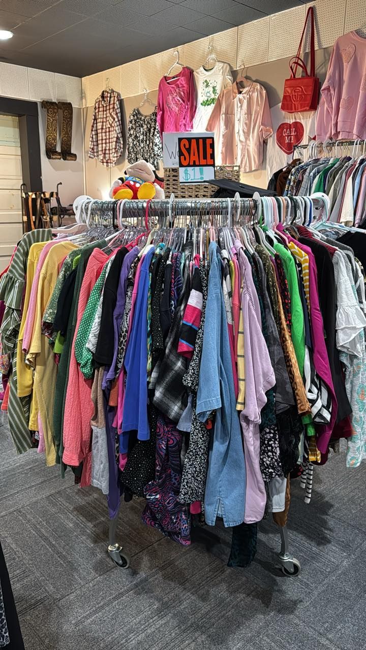 Clothing racks packed with colorful garments in a resale shop, with a red sale sign above.