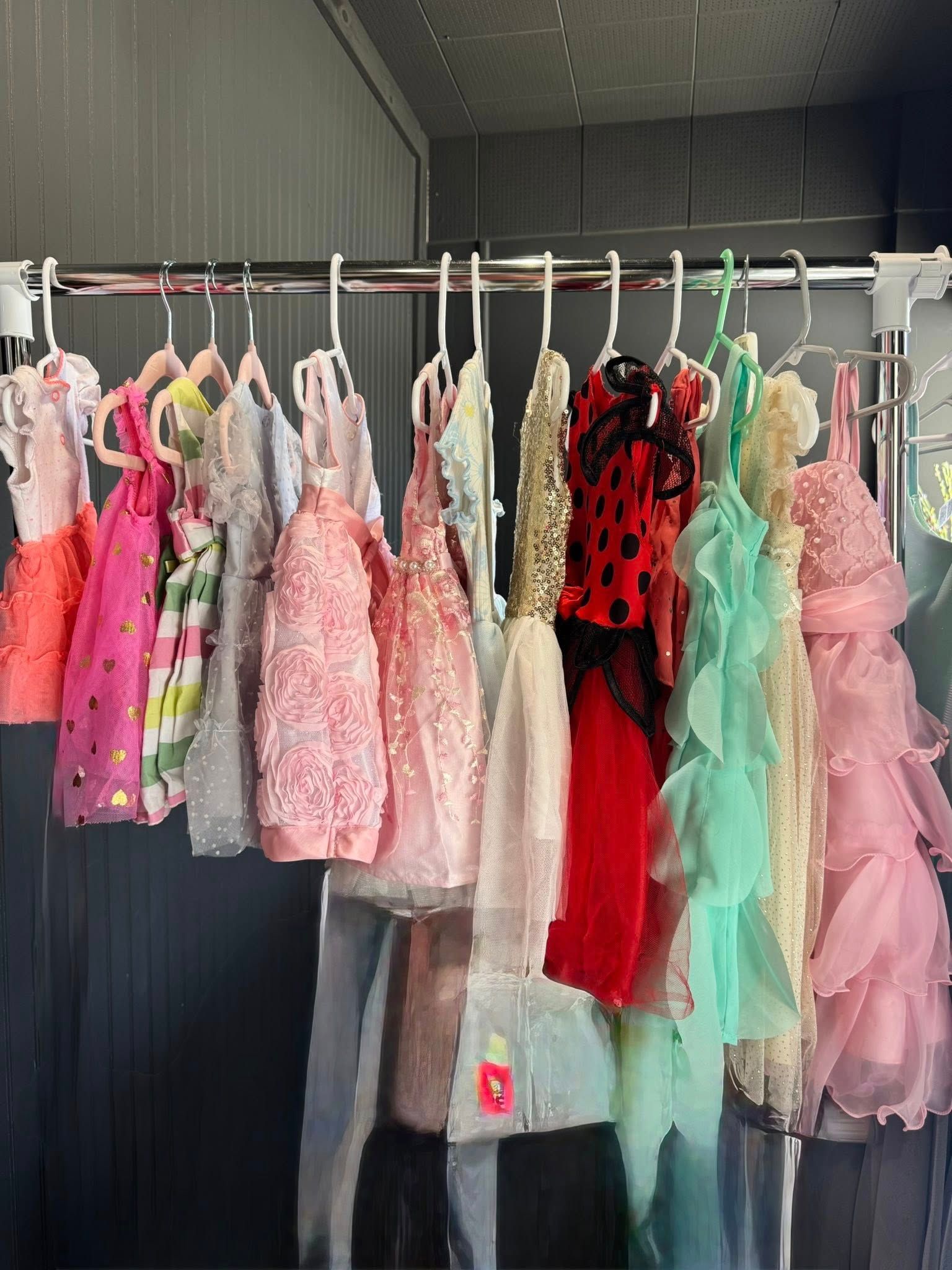 Row of colorful children's dresses hanging on a clothing rack inside a dark storage container.