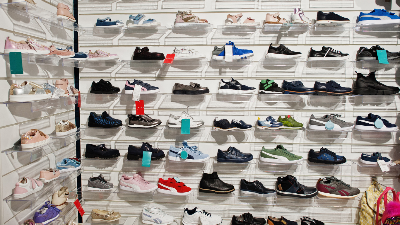 Wall of shelves displaying assorted sneakers and shoes in a store, mostly black, white, red, and blue pairs.