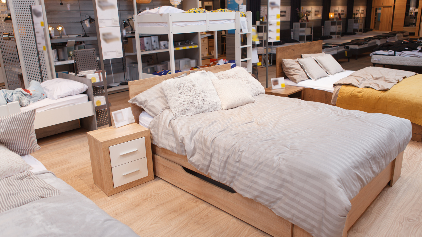 Modern bedroom display with a white bed, wood nightstand, and other mattresses in a furniture store