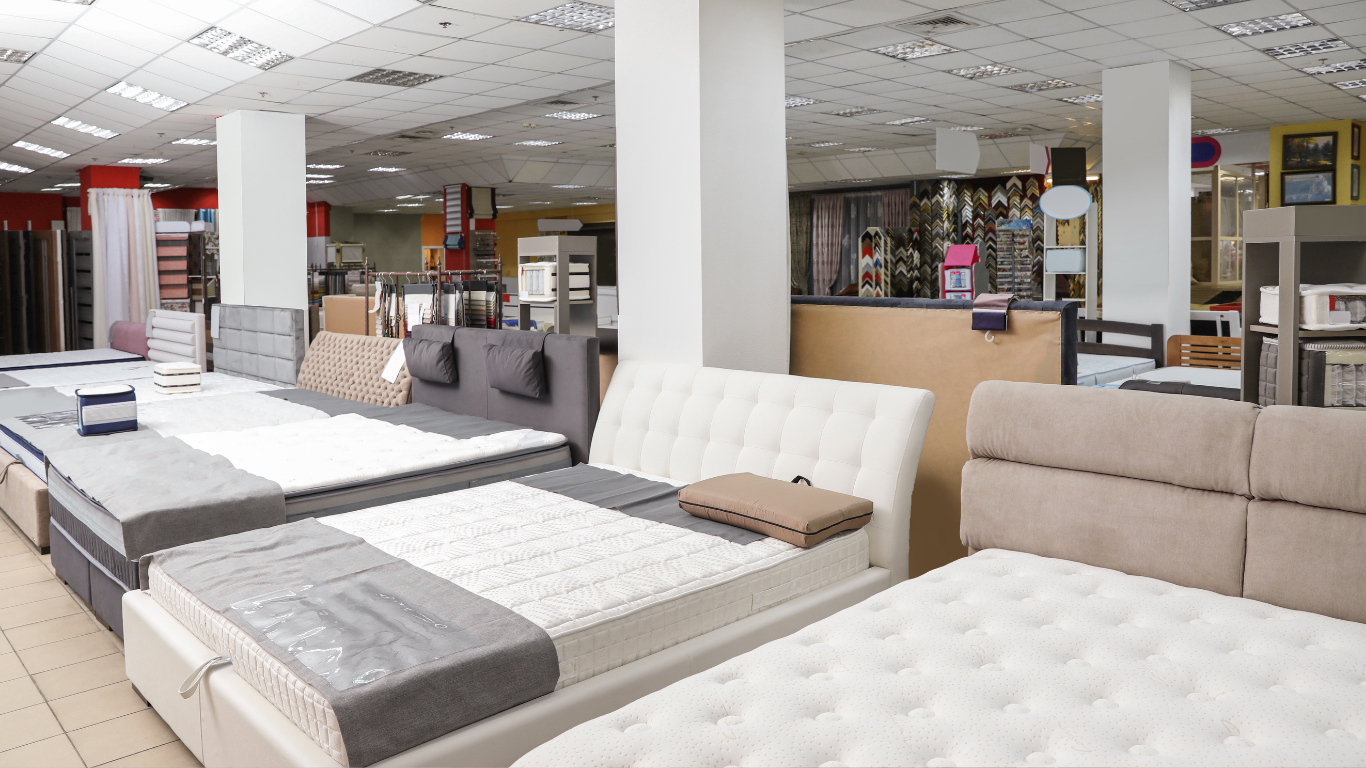 Furniture showroom with several upholstered beds and sofas under bright ceiling lights