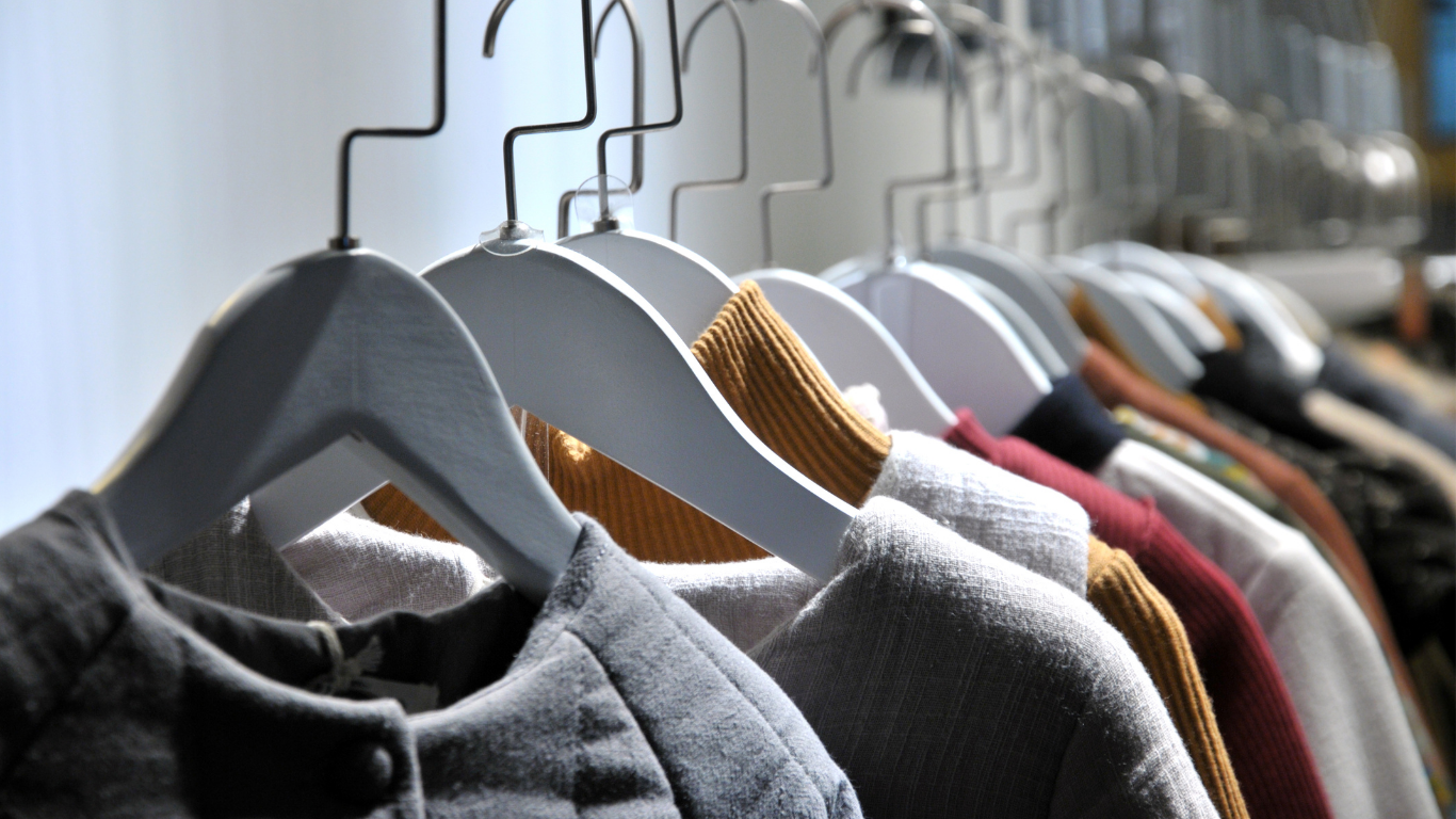 Clothes hanging on wooden hangers on a rack, with gray and colorful garments in soft light