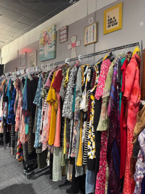 Row of colorful clothing on racks in a retail store, with framed wall art above.